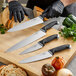 A person in black gloves using a Schraf serrated chef knife to cut bread.