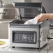 A hand using the Galaxy GVMC10 vacuum packing machine to prepare food on a counter.