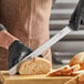 A person in a black glove using a Schraf serrated knife to slice bread.