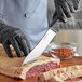 A person in black gloves using a Schraf butcher knife to cut meat on a cutting board.