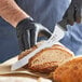 A person in black gloves using a Schraf serrated bread knife to cut a loaf of bread.