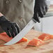A person in black gloves using a Schraf cimeter knife to cut a piece of salmon.