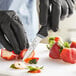 A person in black gloves using a Schraf paring knife to cut strawberries.