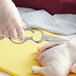 A person in plastic gloves using Mercer Culinary kitchen shears to cut a raw chicken.