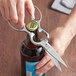 A pair of Mercer Culinary stainless steel multi-purpose shears opening a bottle of beer.