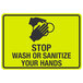 A yellow and black aluminum sign with black text and symbols reading "Stop / Wash Or Sanitize Your Hands"