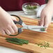 A person using Mercer Japanese Steel Multi-Purpose Shears to cut green onions on a cutting board.