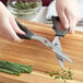 A person using Mercer Culinary kitchen shears to cut green onions on a cutting board.