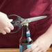 A person uses Mercer Culinary Japanese steel kitchen shears to open a beer bottle.