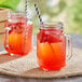 Two Acopa Rustic Charm mason jars filled with orange liquid and strawberries.