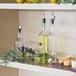 A shelf with Tablecraft glass oil and vinegar bottles next to lemons.
