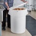 A man putting potatoes in a white round ingredient storage bin.