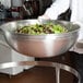 A person holding a Vollrath stainless steel mixing bowl filled with green and red lettuce at a salad bar.