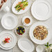 A table set with Acopa Condesa white porcelain plates and bowls with food and drinks.