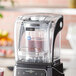 An AvaMix sound enclosure on a blender filled with fruit and juice on a counter.