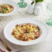 A plate of pasta with mushrooms and cheese in an Acopa pearl white scalloped wide rim porcelain bowl.