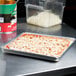 An American Metalcraft square deep dish pizza pan filled with pizza on a counter.