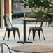 A Lancaster Table & Seating round table top with a textured metal finish on a patio with chairs.