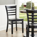 A Lancaster Table & Seating black wood ladder back chair with a black seat at a table in a restaurant.