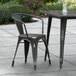 A Lancaster Table & Seating black metal arm chair on a table outside on a patio.