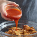 A person pouring Frank's RedHot Sriracha Chili Sauce onto a bowl of chicken wings.