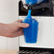 A person pouring blue liquid from a Stoelting frozen beverage machine into a plastic cup.