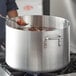 A person stirring food in a silver Choice aluminum sauce pot on a counter.