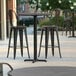 A Lancaster Table & Seating Excalibur bar height table with black chairs on a patio.
