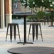 A Lancaster Table & Seating round counter height table with black stools on a patio.