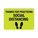 A yellow sign with black text and footprints that says "Thanks For Practicing Social Distancing"