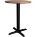 A Lancaster Table & Seating round wooden table with a black cross base.
