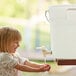 A little girl using a white round Choice hand washing dispenser to wash her hands.