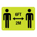A yellow rectangular sign with black figures of two people and text reading "Please Practice Social Distancing" and "6 Ft. / 2 M"