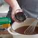A hand using a whisk to mix Knorr Ultimate Beef Bouillon in a bowl of brown liquid.