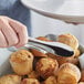 A person using Acopa stainless steel tongs to serve a muffin.