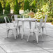 A white Lancaster Table & Seating outdoor table with four white chairs on a patio.