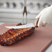 A gloved hand uses a Choice curved stiff boning knife with a brown handle to cut meat.