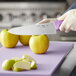 A person in gloves cutting a yellow apple with a Choice 8" Chef Knife with a purple handle.