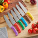 Several Choice chef knives with different colored handles on a cutting board.