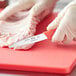A person in gloves using a Choice serrated paring knife to cut meat on a red cutting board.