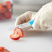 A person in gloves uses a Choice 3 1/4" smooth edge paring knife with a neon blue handle to cut a strawberry.