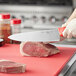 A person using a Choice 10" chef knife to cut raw meat on a red cutting board.