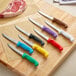 A group of Choice serrated utility knives with colorful handles on a cutting board.