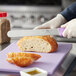 A person cutting a loaf of bread with a Choice serrated bread knife on a purple cutting board.