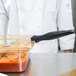 A person in a white coat using a Vollrath solid oval spoodle to scoop red sauce from a glass container.