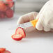 A person in gloves using a Choice smooth edge paring knife to cut a strawberry.