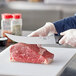 A person cutting raw meat on a cutting board with a Choice cimeter knife.