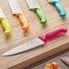 A Choice chef knife with a neon orange handle on a wooden surface.