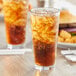 A Pasabahce stackable beverage glass filled with soda and ice on a table with a burger.