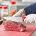 A person cutting raw meat with a Choice 8" Chef Knife with a red handle.